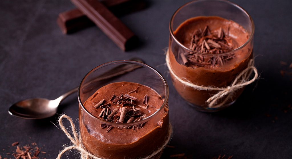 Imagem uma colher e dois potinhos de sobremesa com mousse de chocolate.